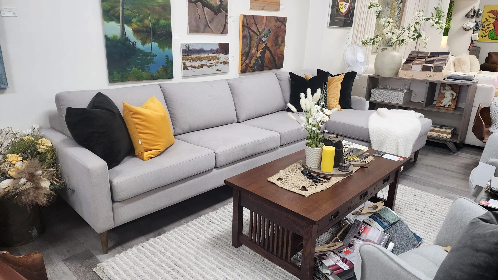 A grey sectional and a mission-style coffee table in the showroom, with paintings by local artists