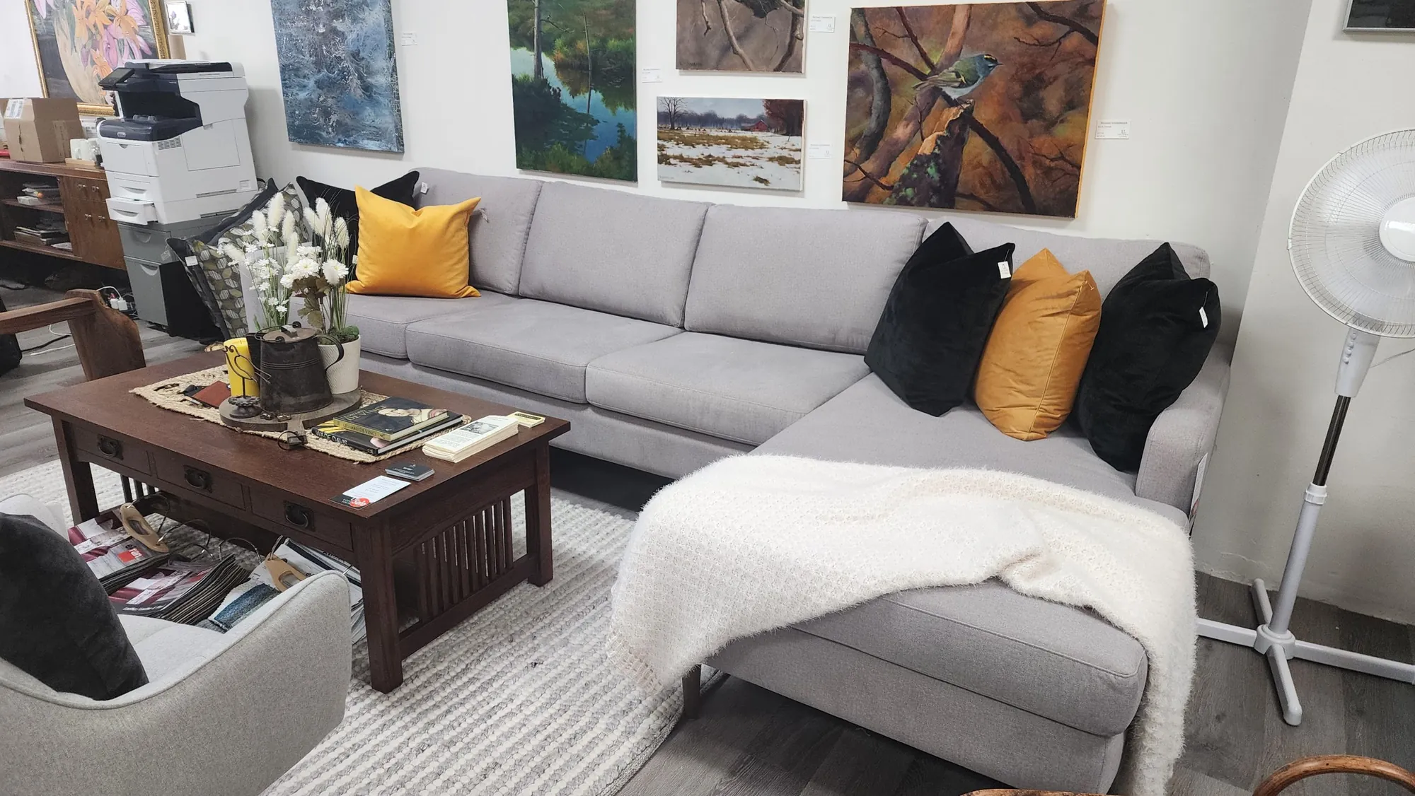 A grey sectional with yellow and black cushions in the showroom, with paintings above